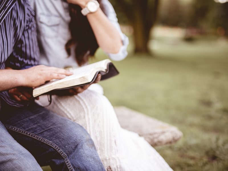 Closeup shot couple sitting park reading bible with blurred background